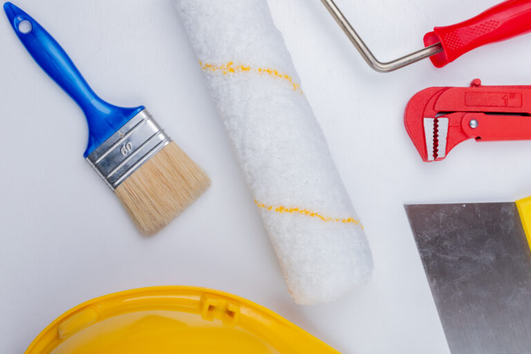 close-up view of construction tools as paint brush and roller safety helmet pipe wrench and putty knife on white background